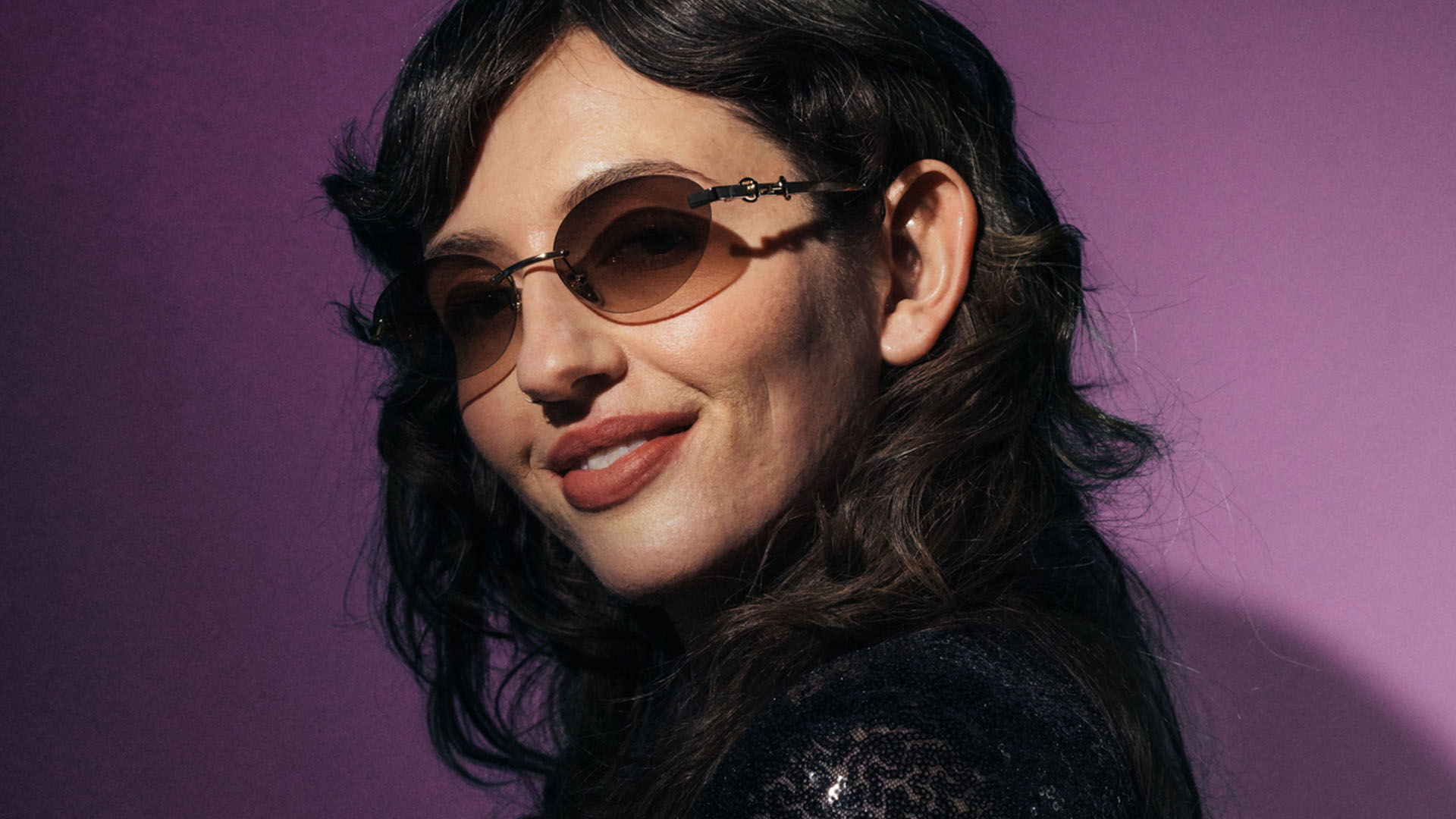 Nainen merkkiaurinkolasit p&auml;&auml;ss&auml; lilalla taustalla